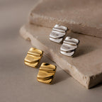 Two pairs of Bold Square Wave Studs in gold and silver are displayed on textured beige stone tiles, perfect for those who love minimalist jewelry.