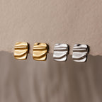 Two pairs of Bold Square Wave Studs, one in gold and one in silver, displayed on textured beige paper—a refined touch for any luxury jewelry lover.