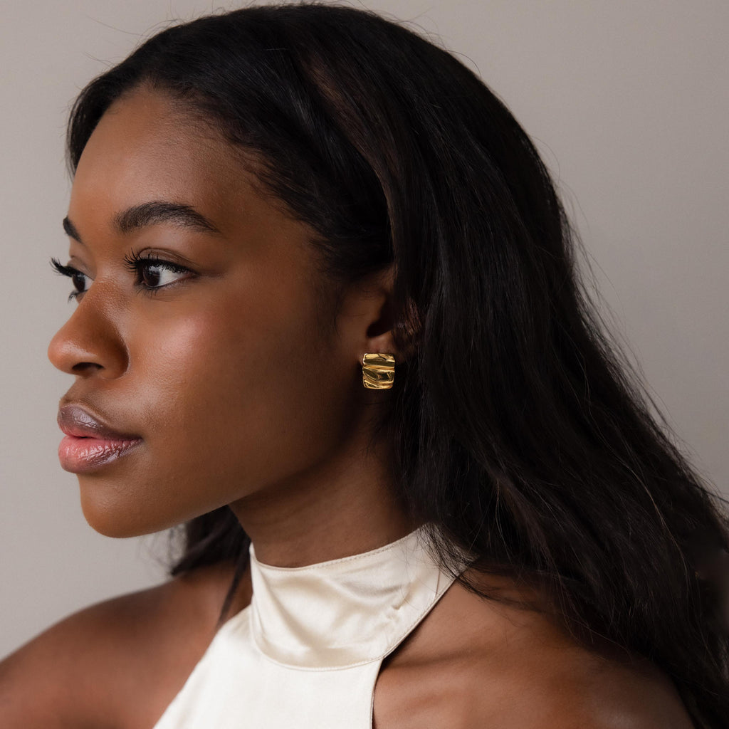 A woman gazes to the side, elegantly showcasing Bold Square Wave Studs.