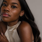 Woman with long hair wears a sleeveless cream top and Vintage Oval Black Studs, looking at the camera.