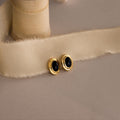 Vintage Oval Black Studs—gold stud earrings with black oval stones—make a chic statement on a beige fabric ribbon and are perfect for elevating any look with timeless charm.