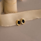 Vintage Oval Black Studs—gold stud earrings with black oval stones—make a chic statement on a beige fabric ribbon and are perfect for elevating any look with timeless charm.