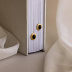 The Vintage Oval Black Studs are displayed against a closed white book with soft fabric beside them, highlighting their retro elegance.