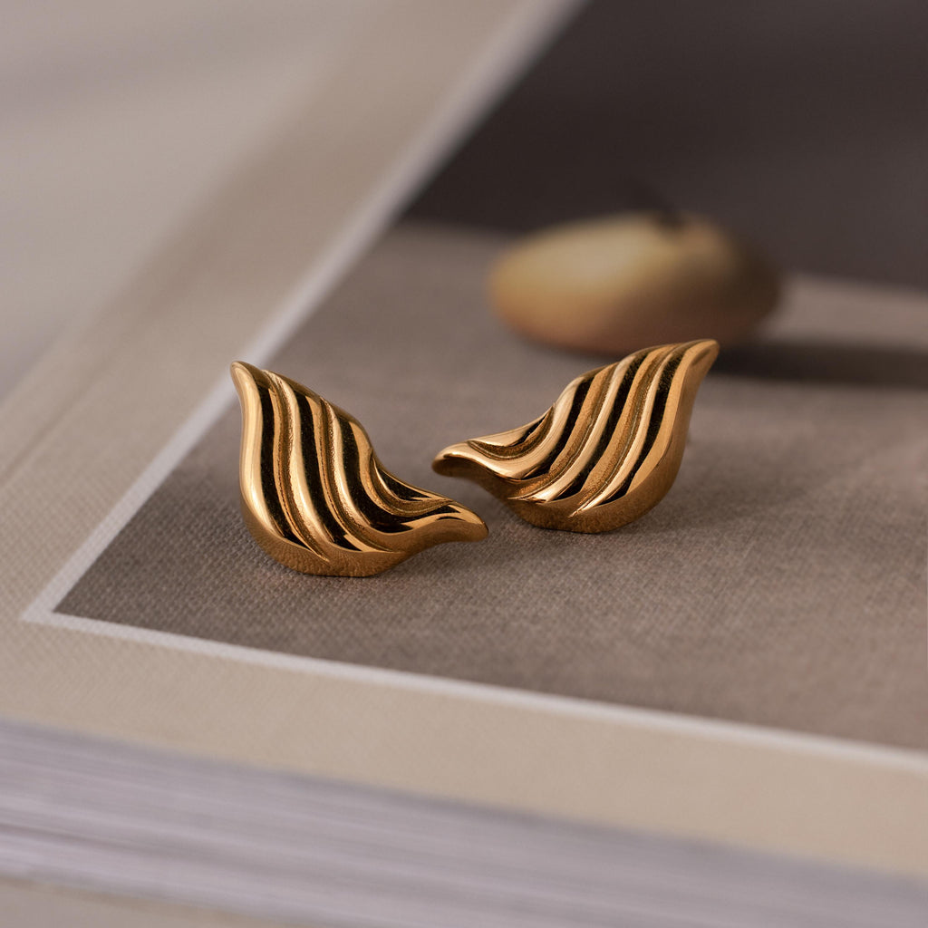 A pair of Bold Wing Studs rests elegantly on a book.