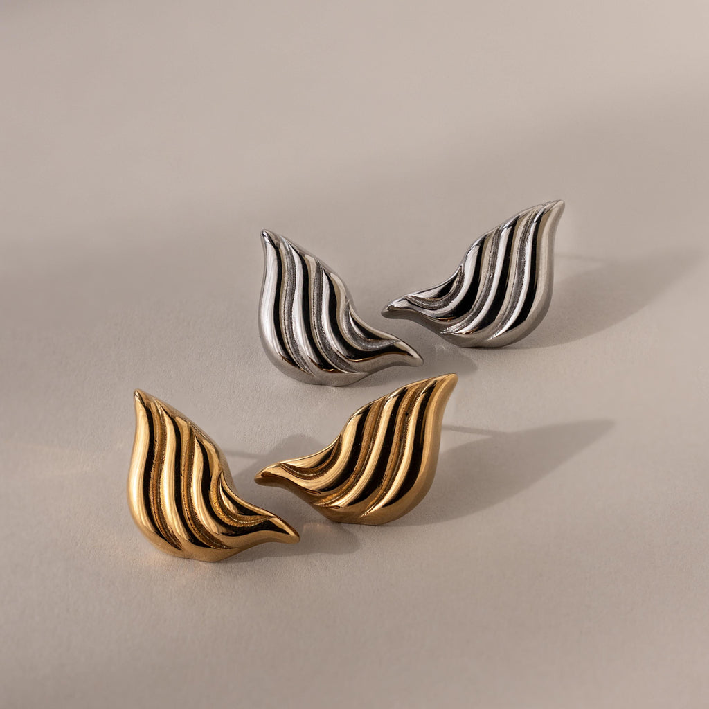 Two pairs of Bold Wing Studs—one in silver, one in gold—are displayed on a neutral background, their wavy, leaf-like shapes echoing the elegance of abstract wing earrings.