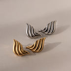 Two pairs of Bold Wing Studs—one in silver, one in gold—are displayed on a neutral background, their wavy, leaf-like shapes echoing the elegance of abstract wing earrings.
