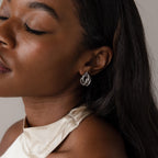 A woman with long dark hair, eyes closed and serene, showcases modern elegance in a cream satin top and Bold Multi Knot Studs.
