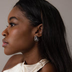 A woman in profile wears Bold Multi Knot Studs—silver, knot-inspired earrings—and a cream halter top, capturing modern elegance against a neutral background.