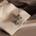 Micro Triple Knot Earrings displayed on a wavy ceramic dish with a book partially visible underneath—an elegant scene that captures the essence of quiet luxury.