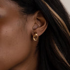 Close-up of a woman's ear wearing Micro Triple Knot Earrings, showcasing quiet luxury with their refined design of small gold overlapping loops.