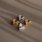 The Bold Triangle Knot Studs—two gold and two silver triangular earrings with engraved lines—are arranged on a neutral, softly lit surface, creating a statement look ideal for lovers of chunky earrings.