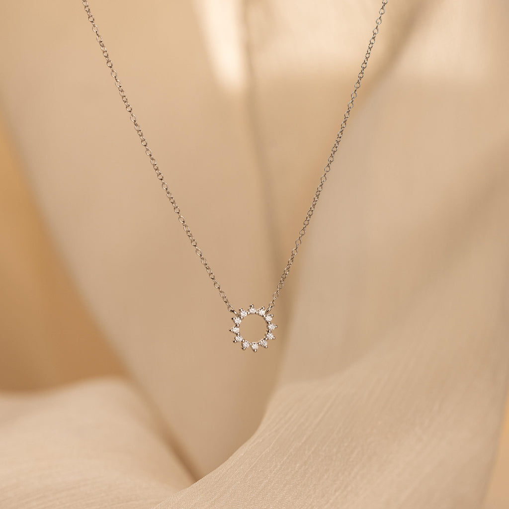 Diamond Sun Necklace with a small sun-shaped pendant accented by sparkling diamonds, shown on a soft beige fabric background.