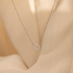 Diamond Sun Necklace with a small sun-shaped pendant accented by sparkling diamonds, shown on a soft beige fabric background.