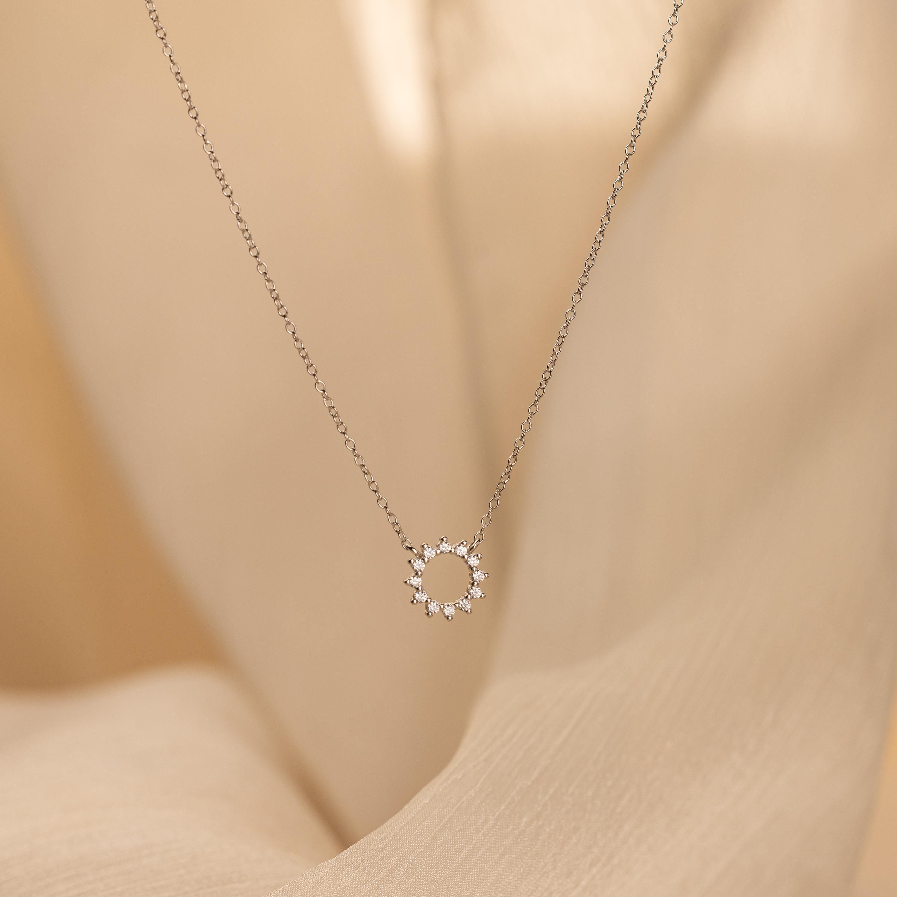 Diamond Sun Necklace with a small sun-shaped pendant accented by sparkling diamonds, shown on a soft beige fabric background.