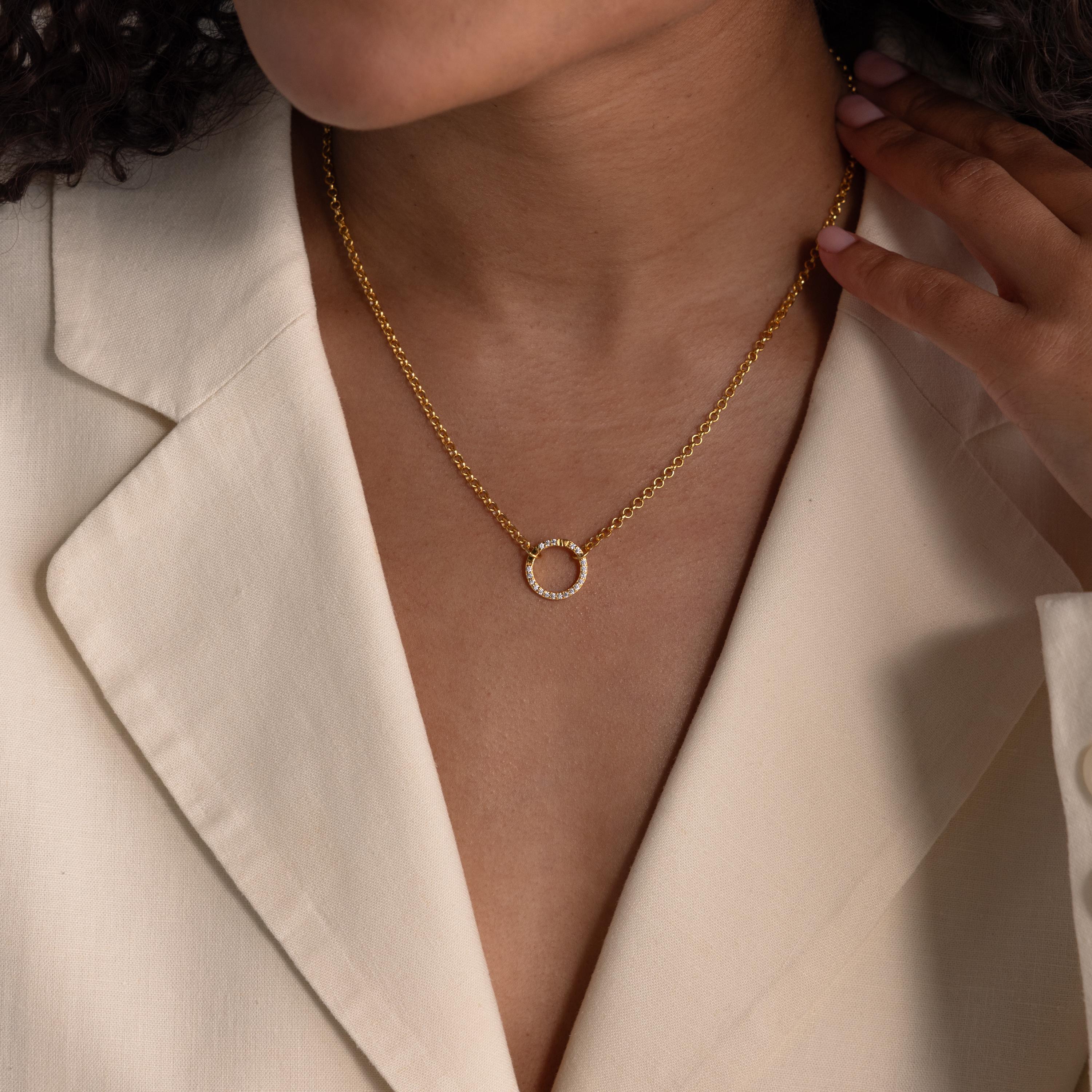 Woman wearing a cream blazer and a gold necklace with a circular Pave Pink Tourmaline Charm Clip pendant, hand touching her collar to showcase this elegant, personalized jewelry piece.