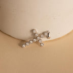 Silver Pave Cross Charm leaning against a vase. The design features multiple round 4mm CZ Diamonds in the shape of a cross with a ribbed bezel setting.