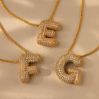 Three Pave Puff Letter Necklaces in 18K Gold, with sparkling pave diamond–studded letter pendants—E, F, and G—shine elegantly on a beige surface, each offering a dazzling gold charm for personalized luxury.