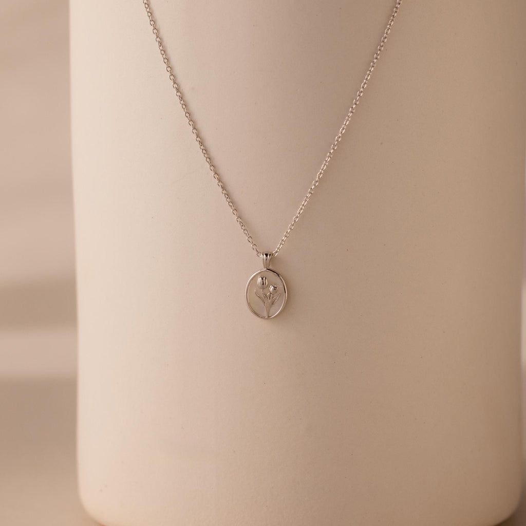 The Pearl Tulip Necklace in Sterling Silver features a round pendant with a delicate tulip design, ideal for floral jewelry lovers and beautifully displayed against a neutral background.