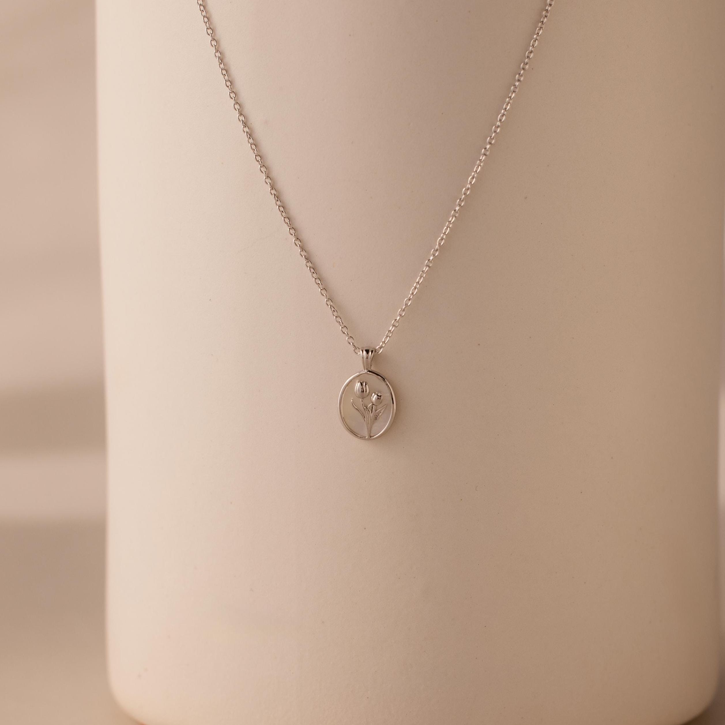 The Pearl Tulip Necklace in Sterling Silver features a round pendant with a delicate tulip design, ideal for floral jewelry lovers and beautifully displayed against a neutral background.