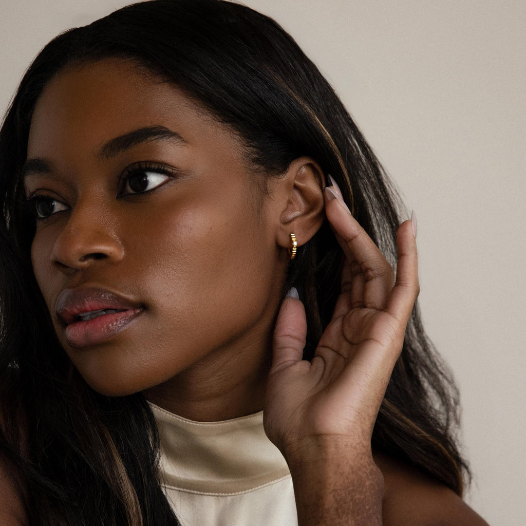 Woman with long dark hair touches her ear and looks to the side, wearing Diamond Ribbed Huggies.