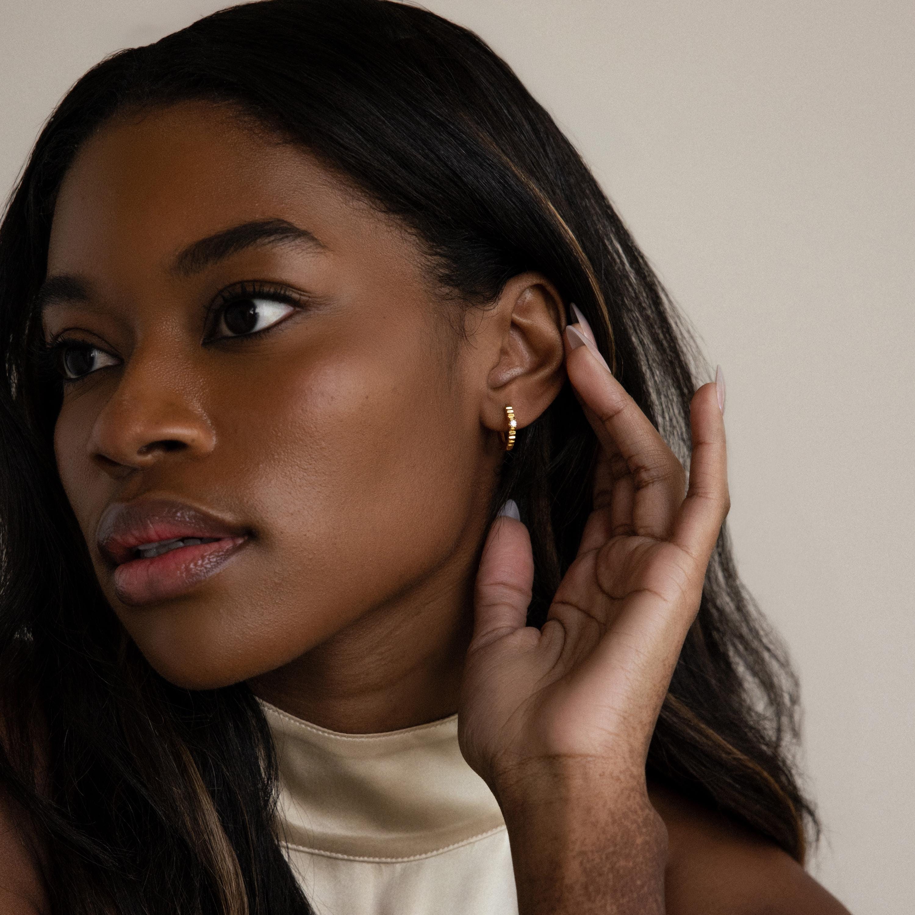 Woman with long dark hair touches her ear and looks to the side, wearing Diamond Ribbed Huggies.