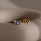 Diamond Ribbed Huggies in silver and gold featuring a ribbed design and small diamonds, shown on a smooth beige surface.