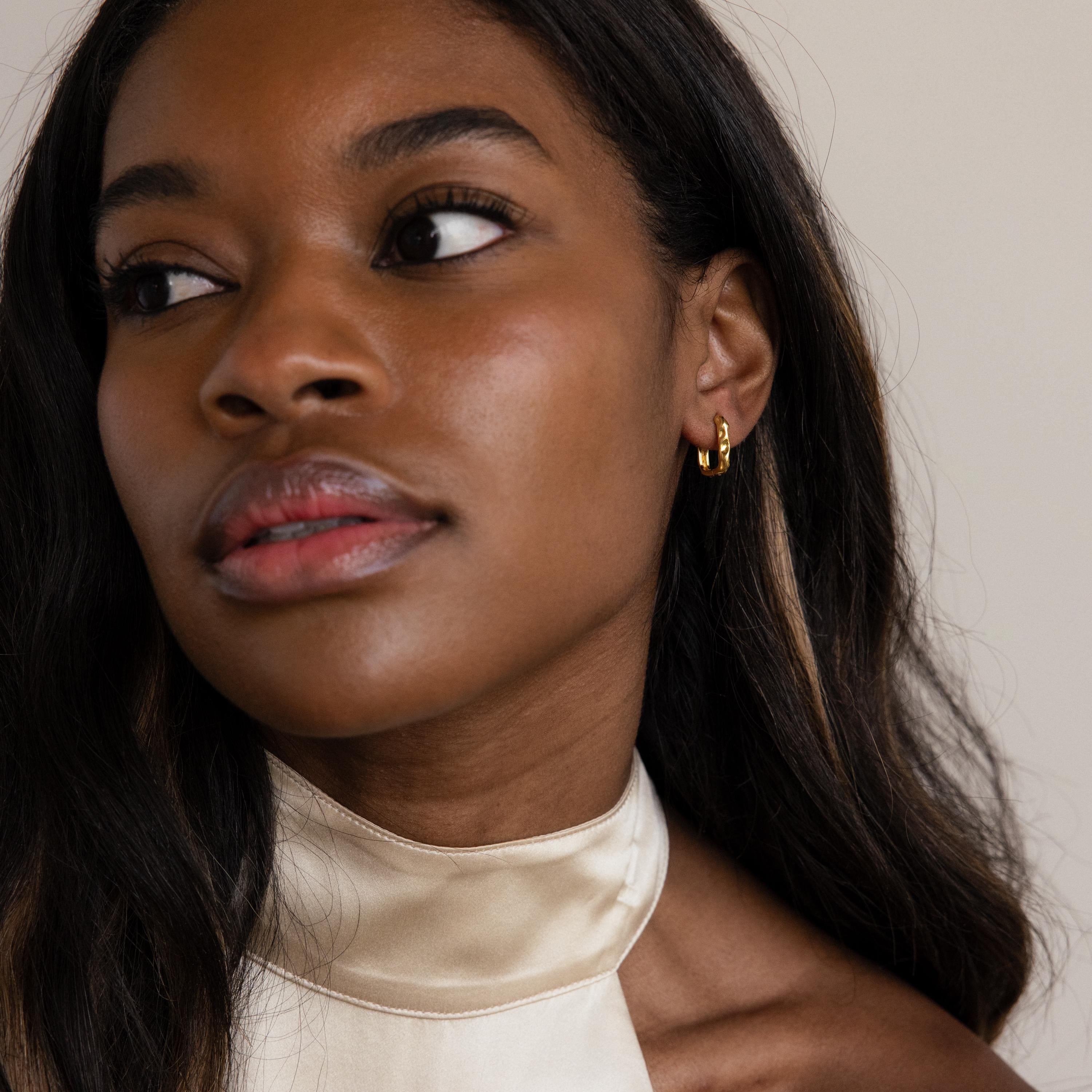 Woman with long dark hair wearing Hammered Rectangle Hoops with a textured finish and a cream satin top, looking to the side.
