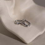 The Hammered Rectangle Hoops feature organic, textured silver shapes and are displayed on a smooth, light-colored sculptural surface.