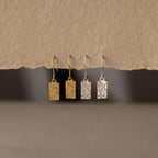 Two pairs of Rectangle Birth Flower Earrings, one gold and one silver, hang on a textured beige background—ideal floral jewelry for anyone who loves unique birth flower earrings.