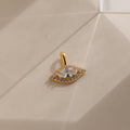 Gold Pave Evil Eye Charm on flat surface. The design features a marquise diamond in the center with pave gemstones surrounding it in the shape of an eye.