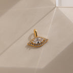 Gold Pave Evil Eye Charm on flat surface. The design features a marquise diamond in the center with pave gemstones surrounding it in the shape of an eye.