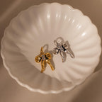 The Diamond Bow Charm in Sterling Silver, inspired by the coquette aesthetic, sparkles with CZ diamonds and crystals on a white scalloped dish.