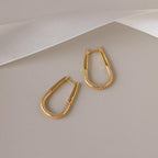 The Bold Pave Oval Hoops, featuring embedded pave diamonds, are displayed on a beige background with a white ribbon accent above.