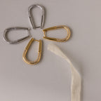 Four Bold Pave Oval Hoops are elegantly arranged like a flower on a light surface, with a textured strip as the stem.