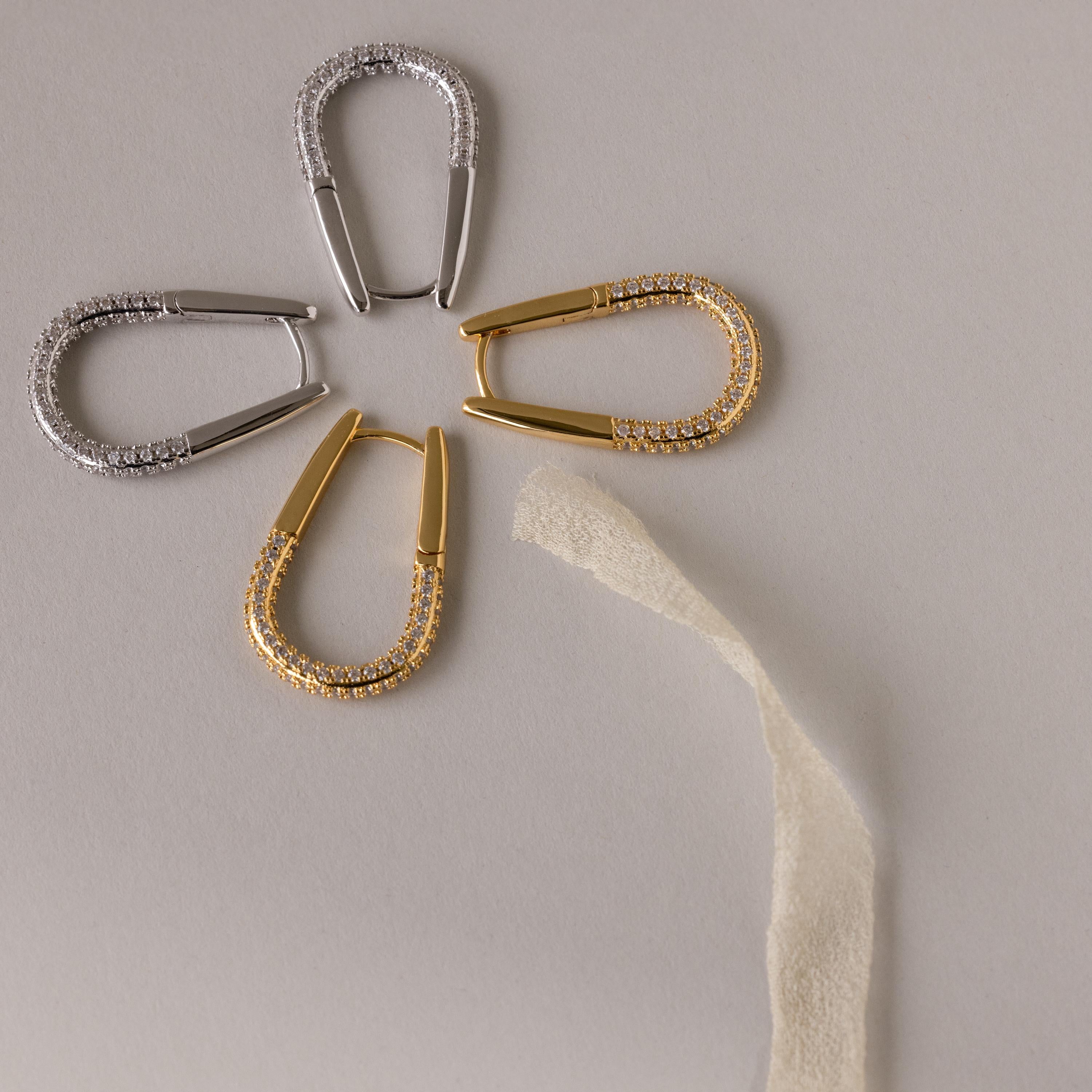 Four Bold Pave Oval Hoops are elegantly arranged like a flower on a light surface, with a textured strip as the stem.