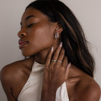 A woman with closed eyes gently touches her neck while wearing the Bold Pave Oval Hoops and a satin halter top.