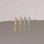 The Bold Pave Oval Hoops set features two pairs of thin, textured statement earrings in gold and silver, displayed on a torn paper background—ideal for adding a touch of sparkle to any outfit.