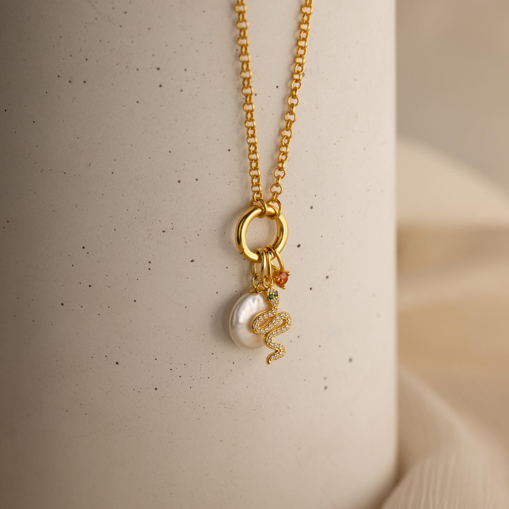 A gold rolo circle necklace with dangling gold snake charm, birthstone charm and pearl charm