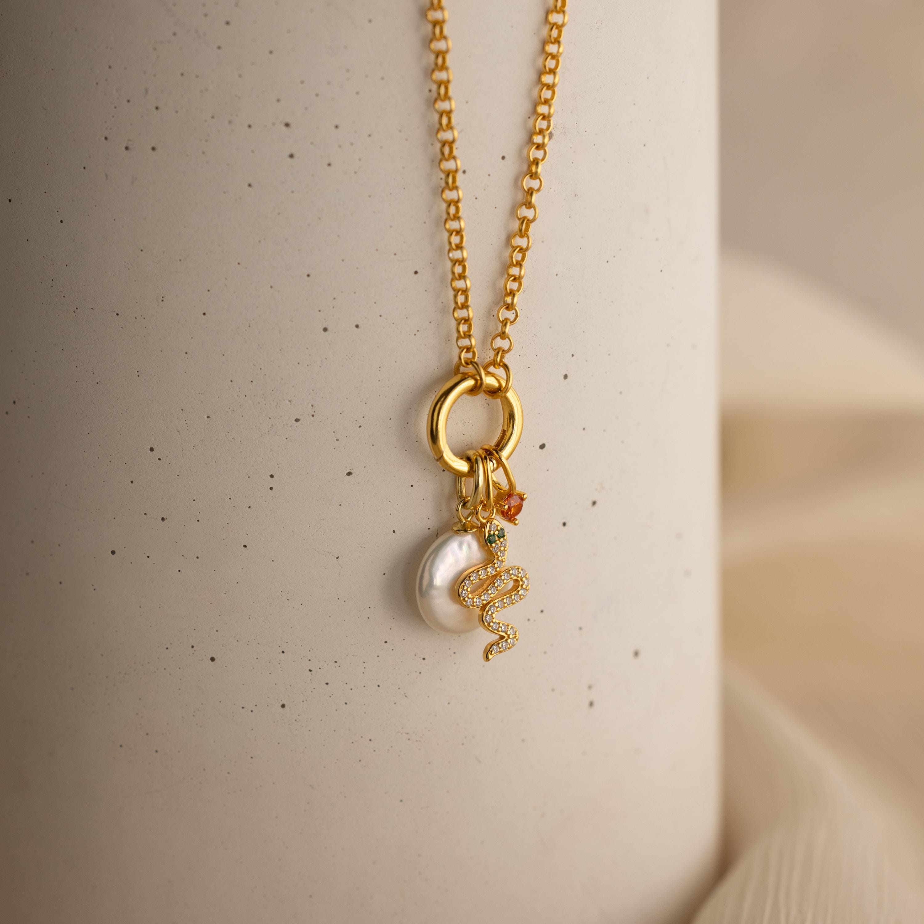 A gold rolo circle necklace with dangling gold snake charm, birthstone charm and pearl charm