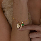 A model wears a satellite chain adorned with a gold diamond snake charm, green birthstone charm and initial charm