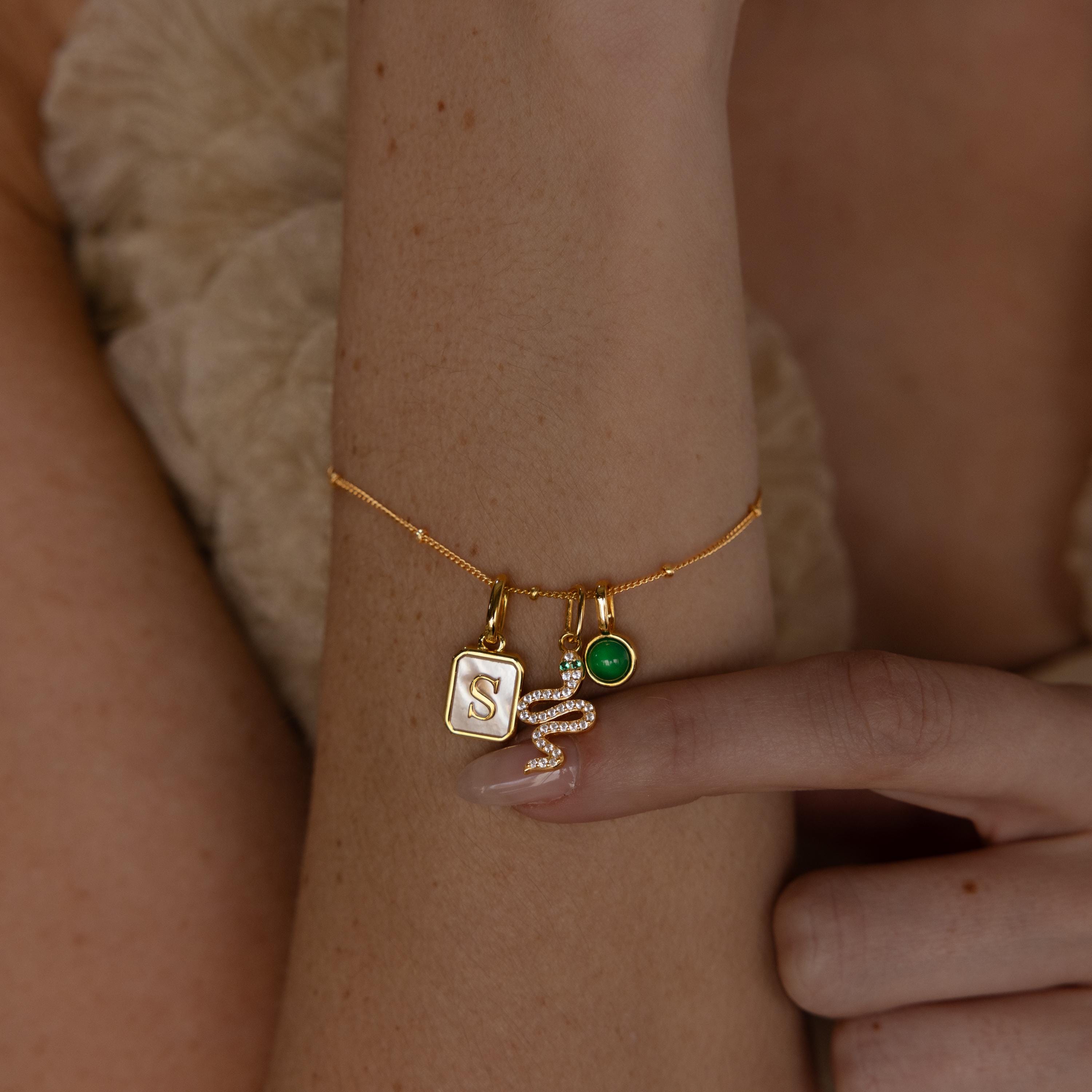 A model wears a satellite chain adorned with a gold diamond snake charm, green birthstone charm and initial charm