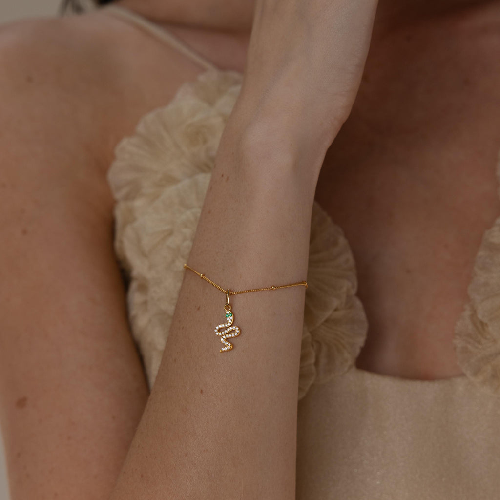 Model wears gold diamond snake charm hanging from a satellite bracelet