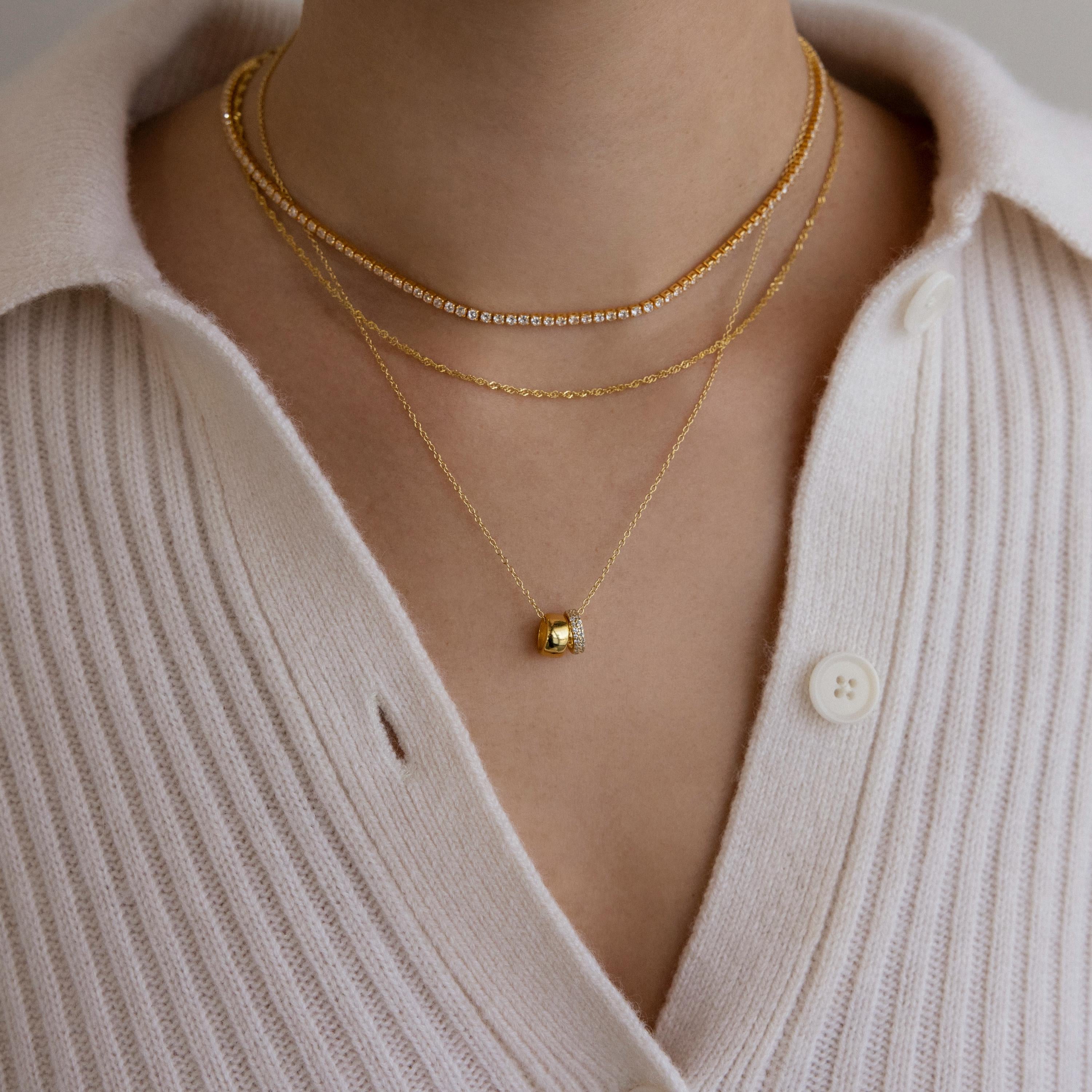 Close-up of a person wearing elegant jewelry: three gold necklaces, including the dainty Pave Duo Circle Necklace, paired with a cream-colored button-up knit top.