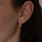 Close-up of a woman's ear wearing Black Diamond Drop Huggies—elegant gold hoops accented with small clear stones.
