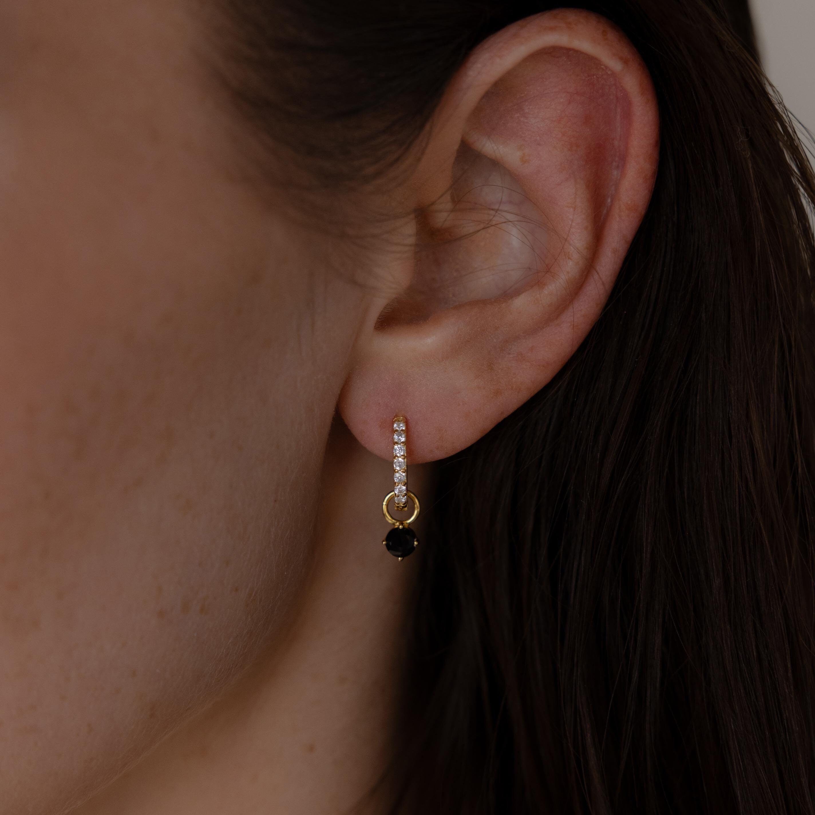 Close-up of a woman's ear wearing Black Diamond Drop Huggies—elegant gold hoops accented with small clear stones.