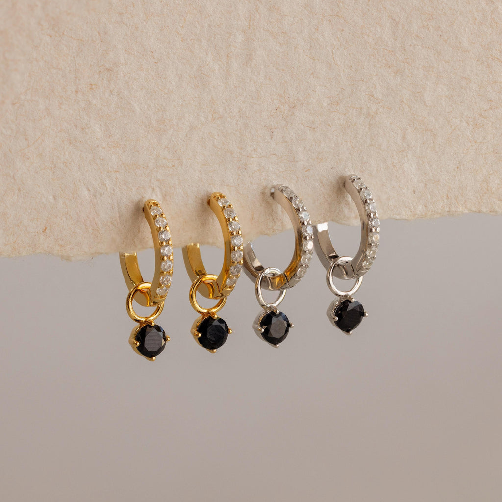 Two gold and two silver hoop earrings, each with clear stones and a dangling black gem, deliver elegance—perfect for those seeking the refined style of Black Diamond Drop Huggies.