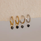 Two gold and two silver hoop earrings, each with clear stones and a dangling black gem, deliver elegance—perfect for those seeking the refined style of Black Diamond Drop Huggies.