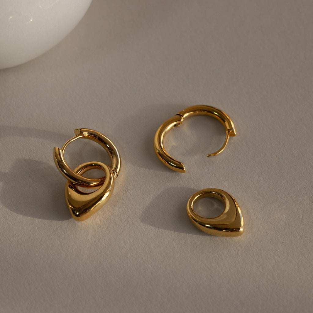 The Bold Teardrop Hoops showcase delicate, teardrop-shaped pendants in a small gold design, offering versatile earrings that catch and reflect light beautifully.