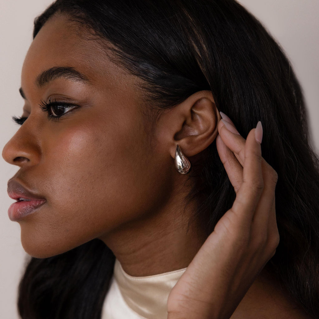 A woman with long dark hair touches her ear while wearing Chunky Tear Drop Studs, shown in a close-up side profile.