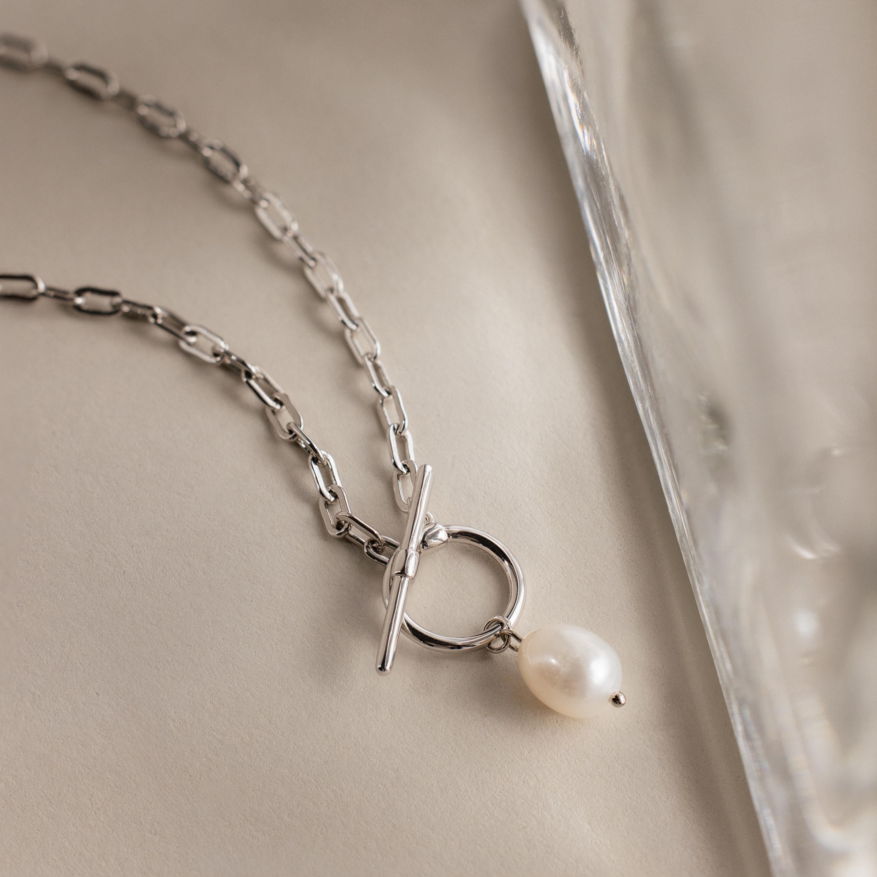 The Paperclip Pearl Toggle Necklace features a single dangling pearl and an elegant toggle clasp, displayed on a neutral surface—ideal for anyone who loves timeless pearl jewelry.